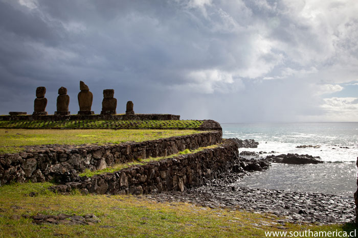Easter Island Statues with dark clouds in the background as well as part of the beach